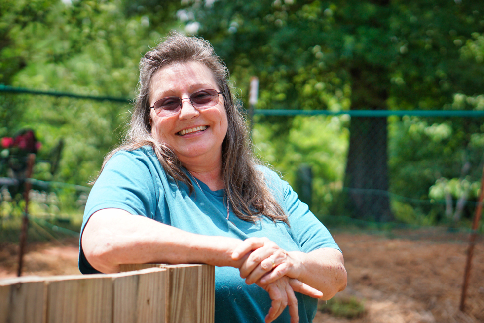 A beauty shot of Tami, resting her arm on the fence around the compost pile