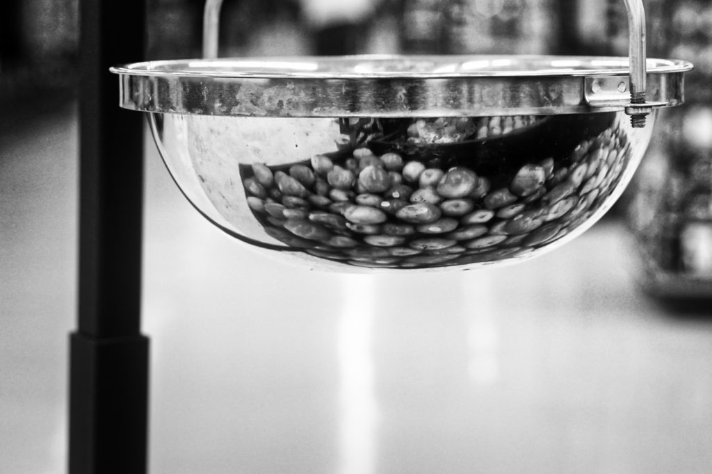 A black and white photo of a chrome produce-weighing scale with a bunch of apples reflected in the chrome. There are a lot of fingerprint smudges on the chrome bowl.