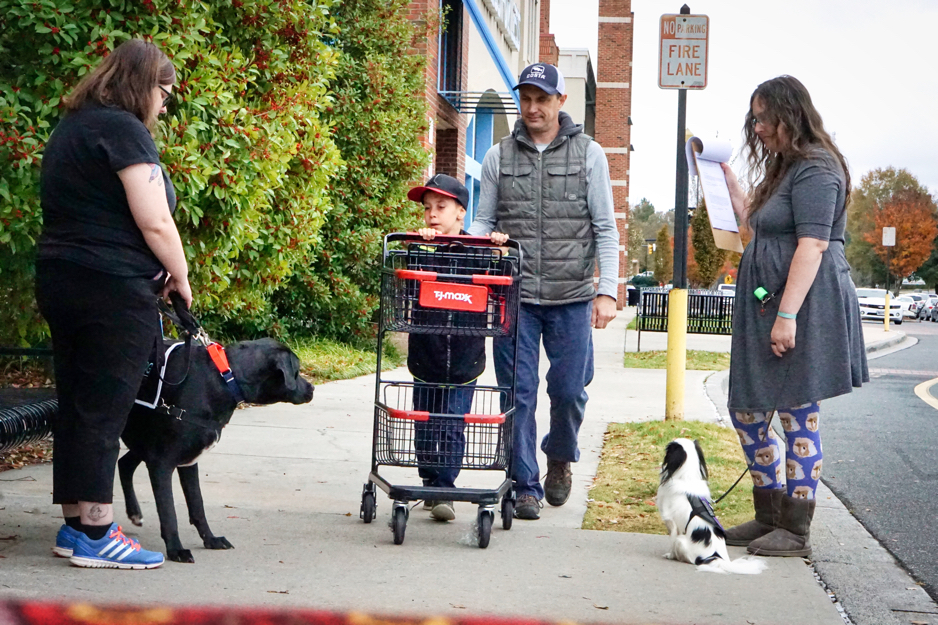 A family pushing a shopping cart passes Kristi with Jax and Veronica with Hestia.