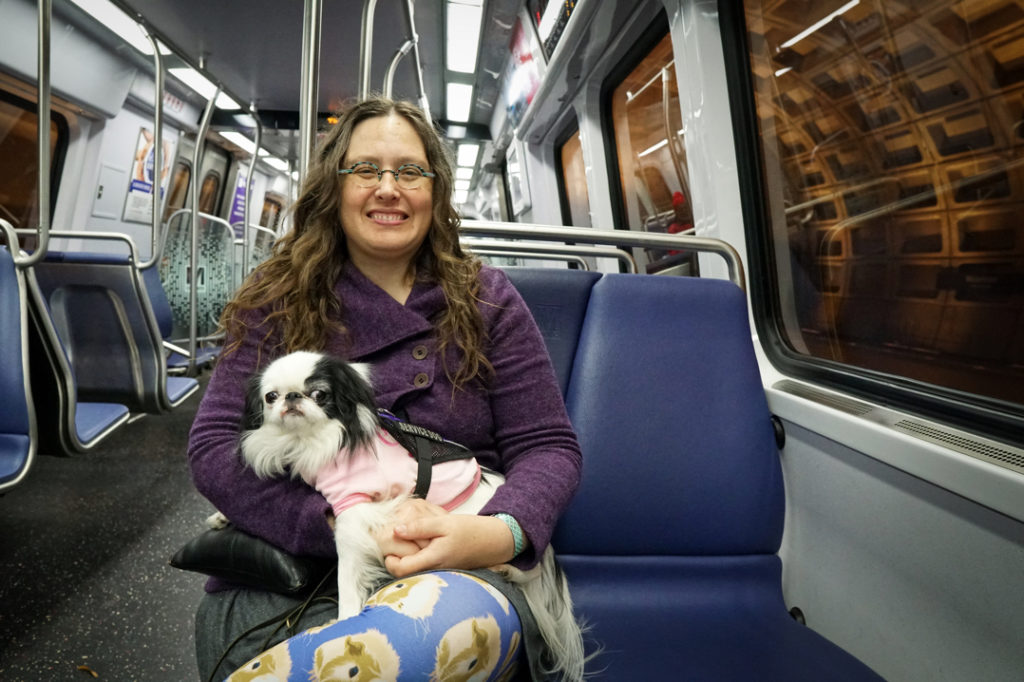 Veronica holds Hestia as they both smile at the camera while sitting on the Metro train.