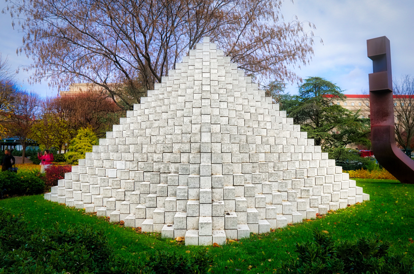 A sculpture of concrete blocks arranged in a pyramid shape. It is very striking, especially the white blocks against the green grass and the blue sky.