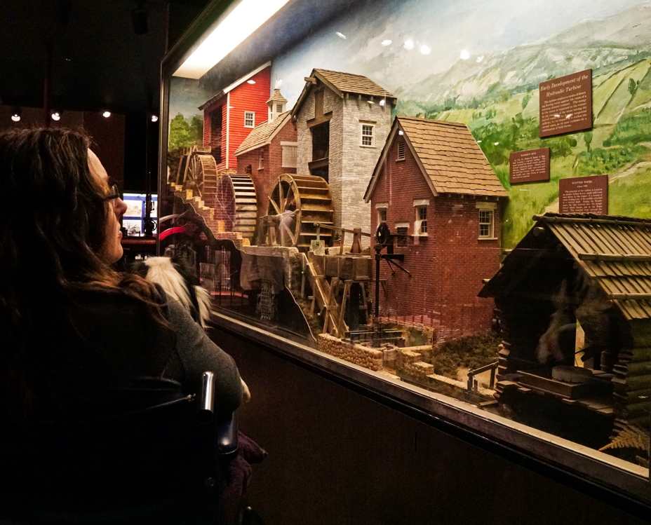 Veronica looks at a diorama of model waterwheels along a village.